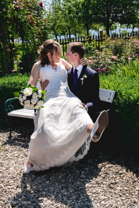 Braut und Bräutigam auf Bank, lachend im Sonnenschein, Hochzeitsfoto, Zwischenmomente | Nina Hrusa Photography
