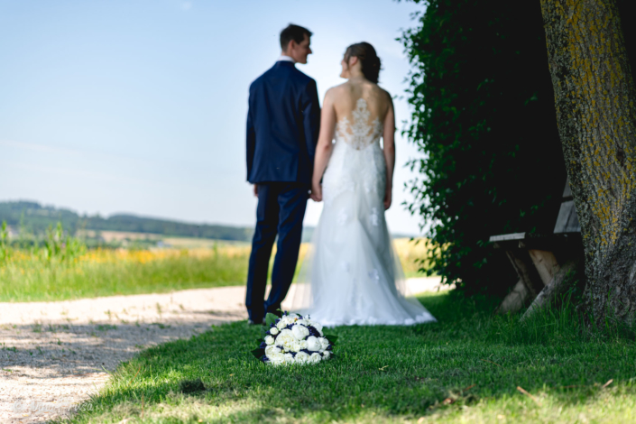 Brautstrauß mit Brautpaar im Hintergrund, Hochzeitsfotografie, Zwischenmomente | Nina Hrusa Photography